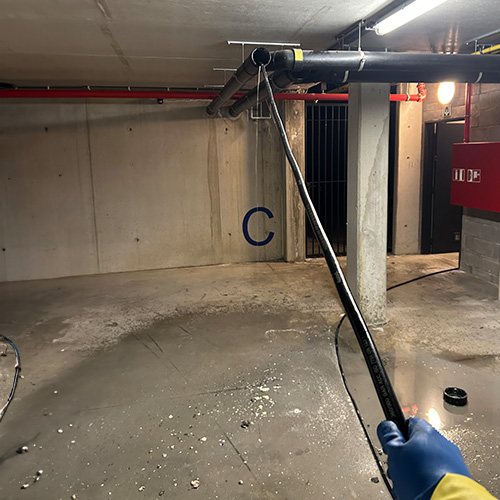 Het reinigen van een rioleringsbuis in een ondergrondse parkeergarage door een specialist